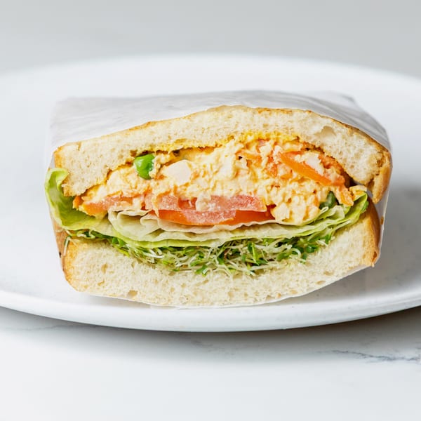 Half a sandwich with chicken salad, lettuce, tomatoes, and sprouts on a white plate.