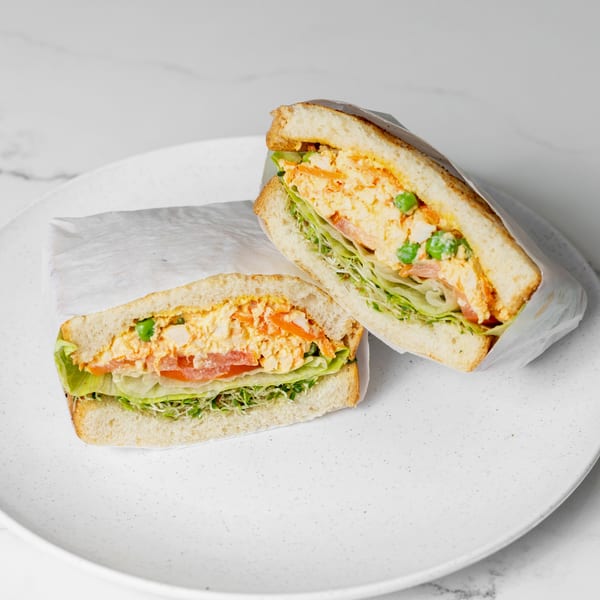 Two halves of a sandwich with chicken salad, lettuce, tomato, and sprouts on a white plate.