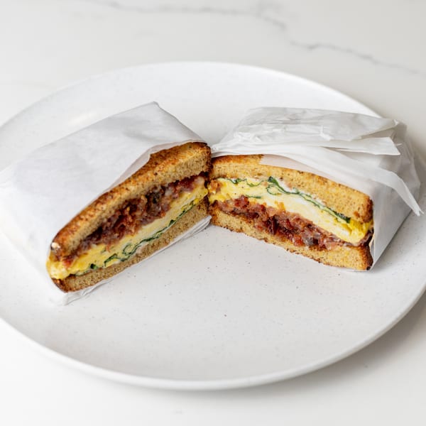 A breakfast sandwich, cut in half and wrapped in paper, sits on a white plate.